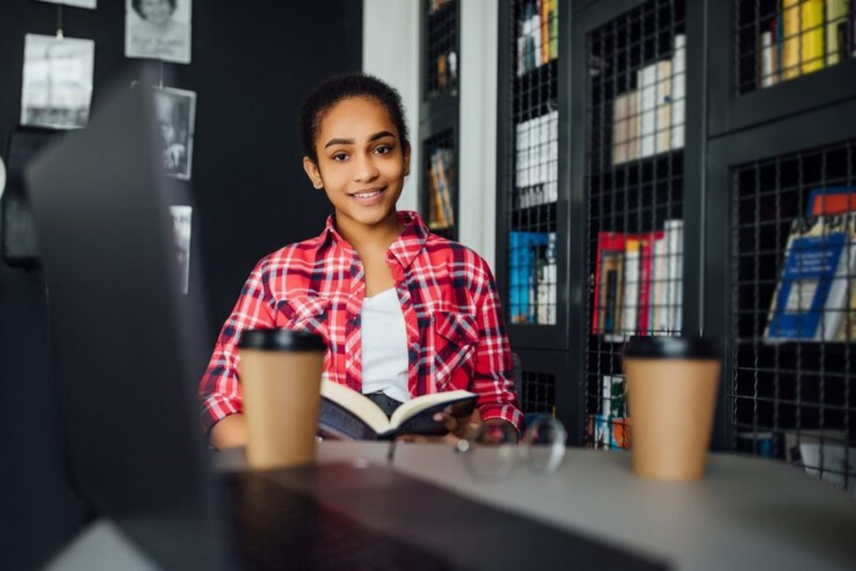 Uma estudante lê o livro sentada dentro da biblioteca 