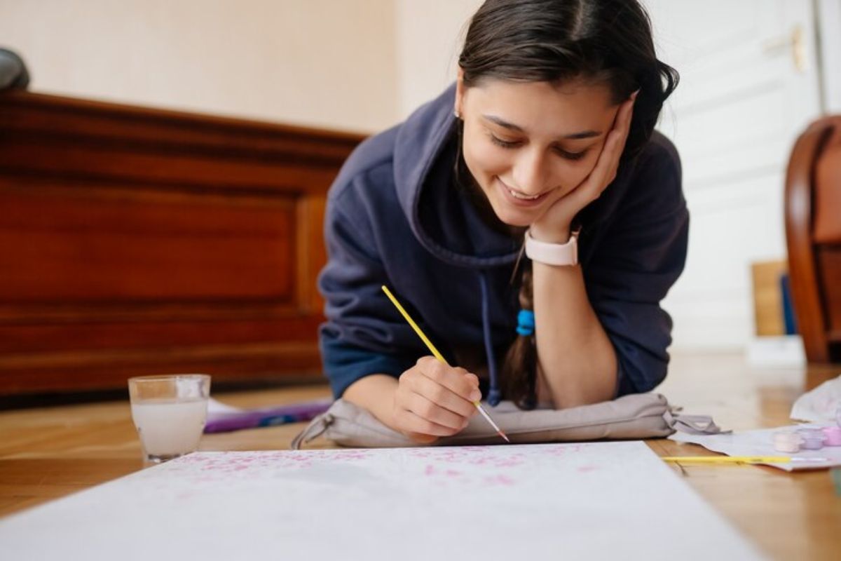 Uma menina está deitada de bruços enquanto escreve em seu caderno os principais pontos da rematrícula FIES 2025