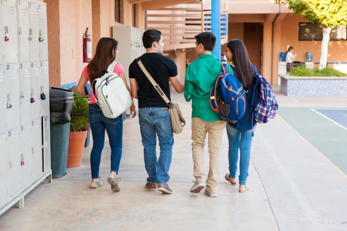 Alguns estudantes no corredor da universidade vistos de costas. Eles conversam sobre a renegociação FIES 2025