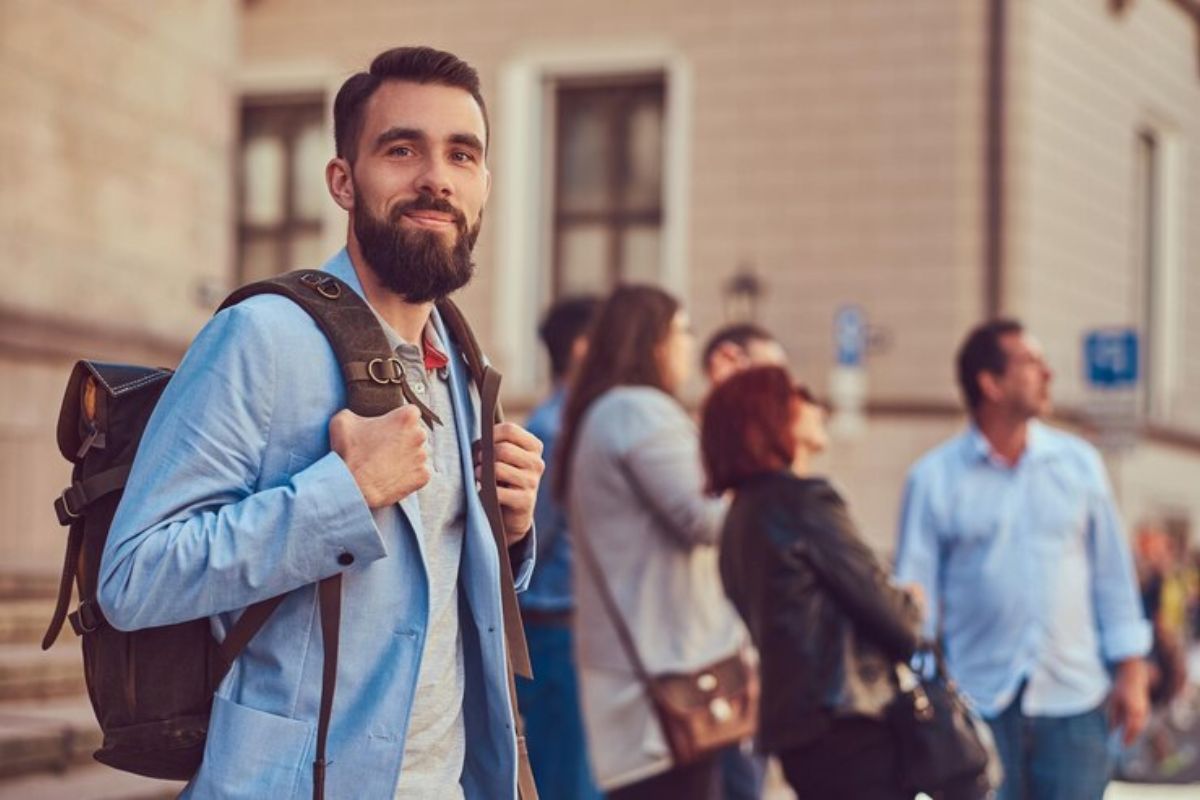 Um estudante segura sua mochila nos ombros. Ao fundo é possível ver alguns de seus colegas 