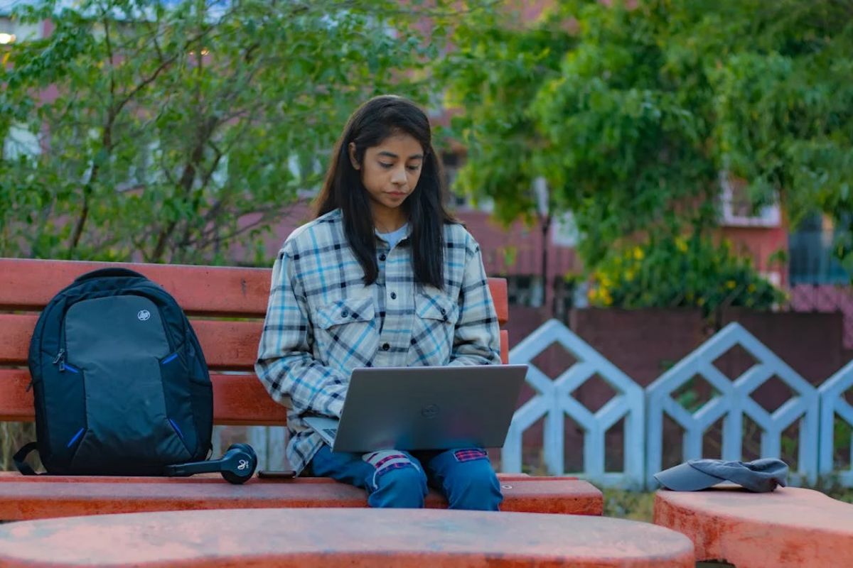 Uma estudante sentada no banco da praça com o notebook no colo