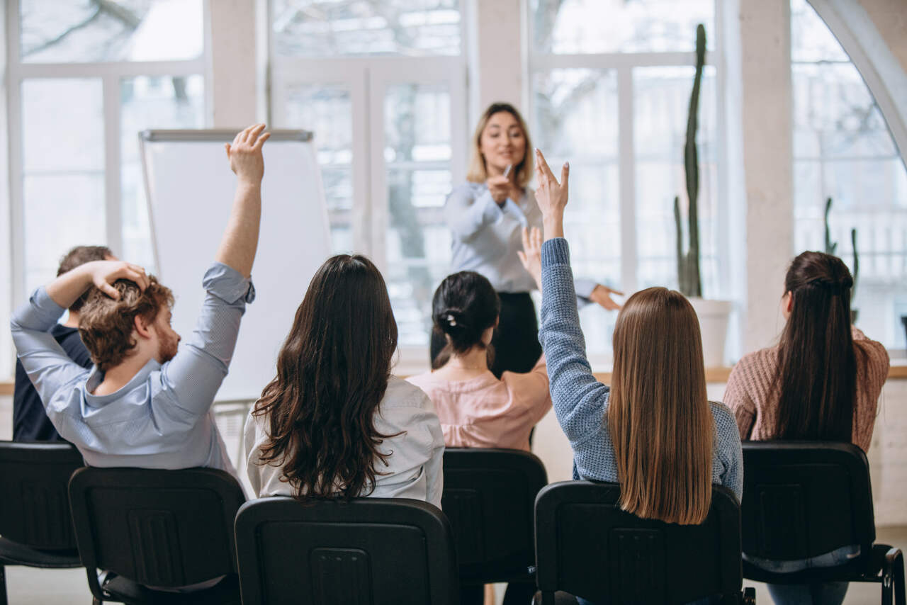 Professora ouve alunos de mãos levantadas na sala de aula 