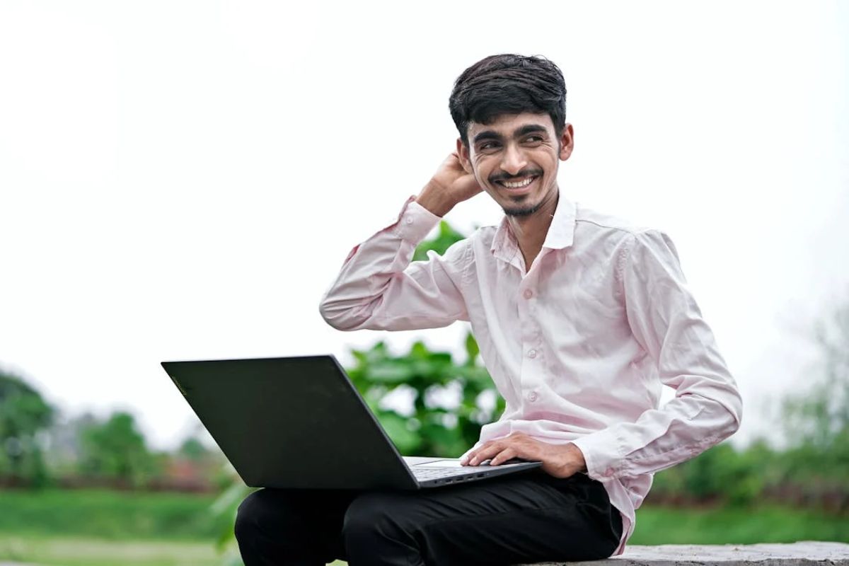 Um estudante ao ar livre com o notebook no colo vendo quais são os critérios para o Fies Social 2025