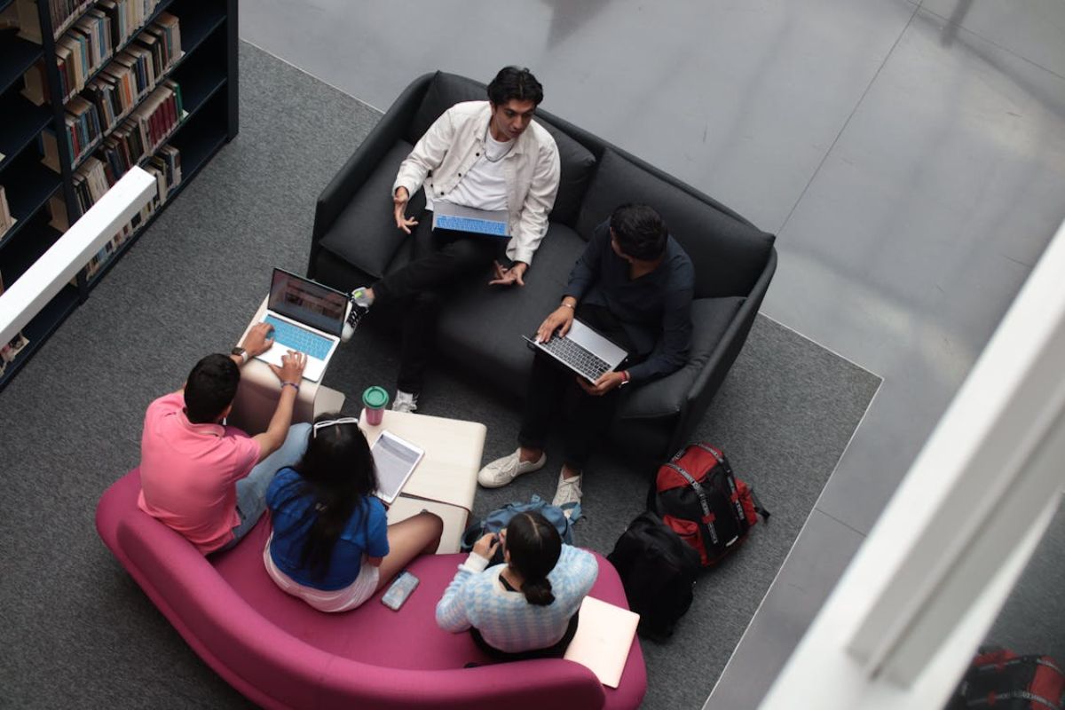 Cinco aluno vistos de cima. Eles estudam juntos para um trabalho de faculdade