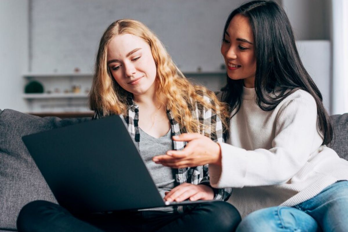 Duas colegas estudam juntas no quarto. Uma delas está com o notebook no colo