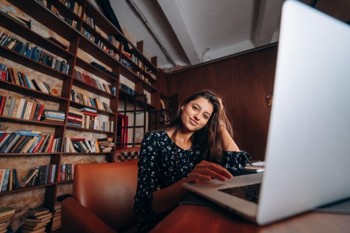 Uma estudante em frente ao seu notebook que está na mesa onde ela apoia o cotovelo. Ela pesquisa quais as melhores faculdades do sul de Minas para conseguir FIES