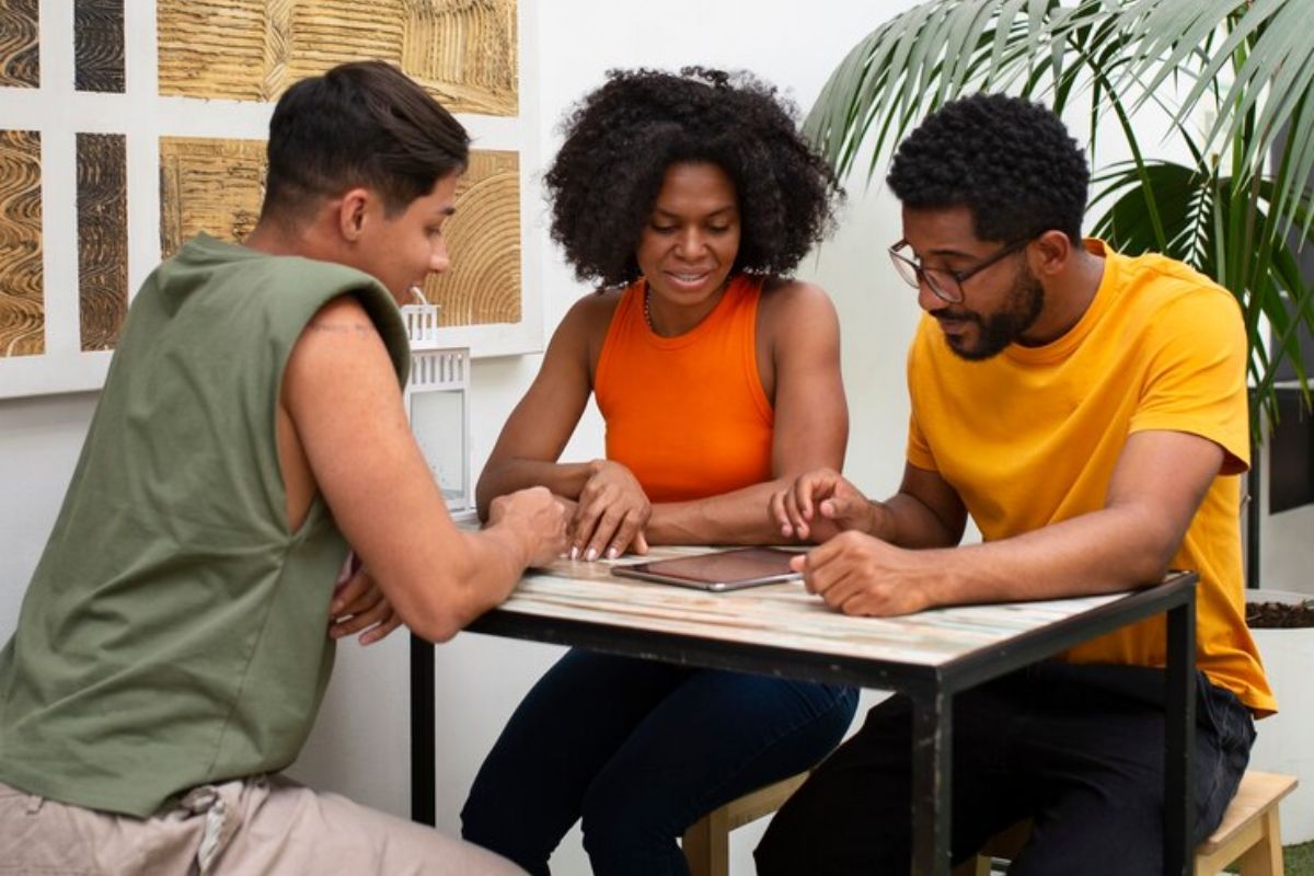 Três estudantes compartilham uma mesa onde fazem o trabalho da universidade juntos