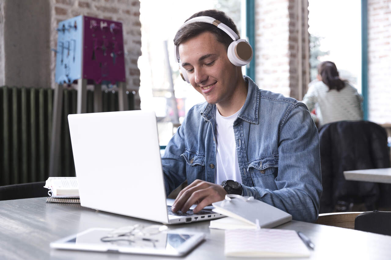 Jovem assiste aula online no notebook usando fones de ouvido